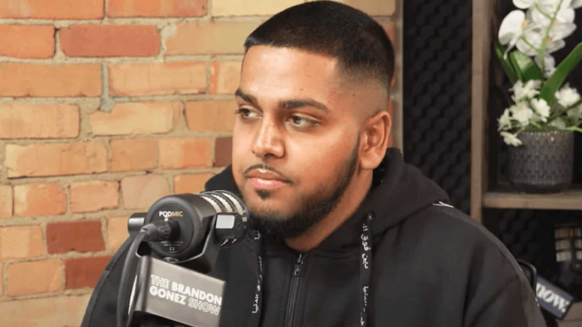 Young man with a short haircut and beard speaking into a microphone during a podcast interview at NOW Toronto studio.