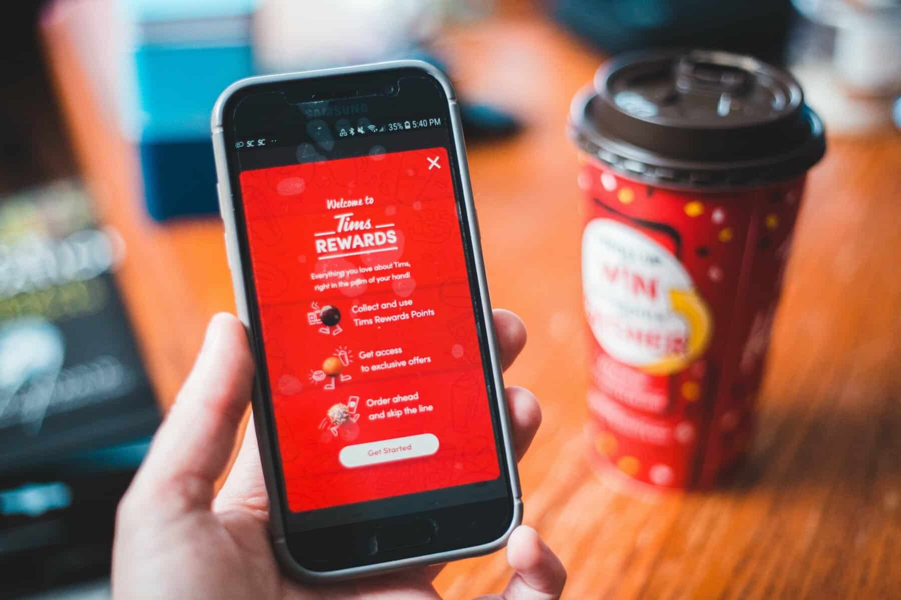 Mobile app showing Tims Rewards program on a smartphone in a coffee shop.