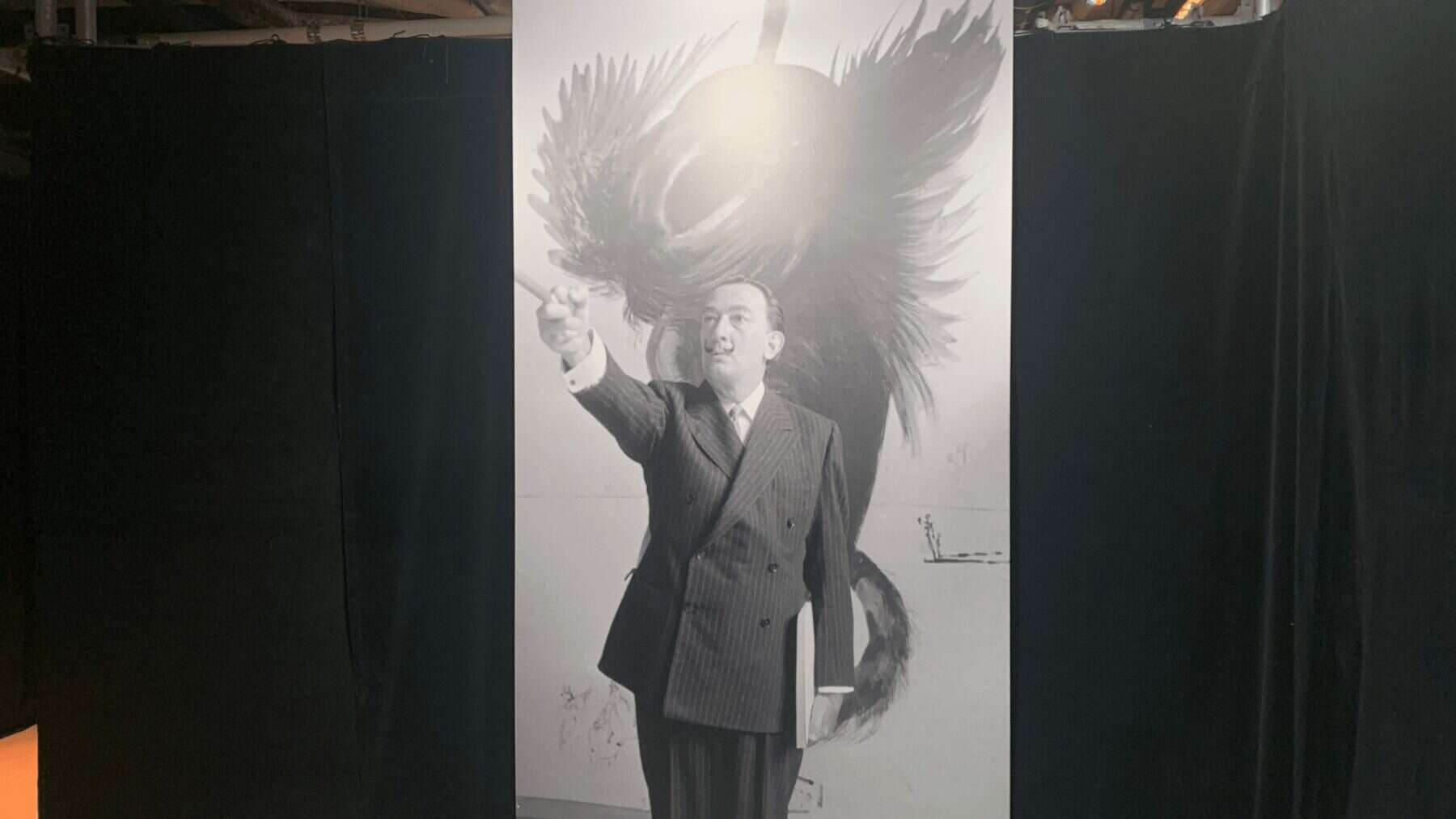 Josephine Baker inspired black and white photo of a man in a pinstripe suit pointing, with a dramatic feathered hat background, displayed at NOW Toronto.