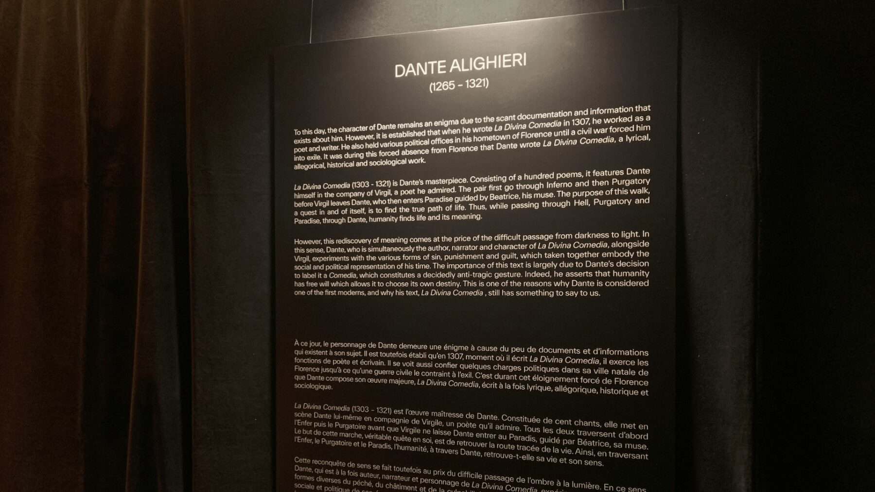 Dark museum exhibit panel about Dante Alighieri and La Divina Comedia, with detailed historical and literary context, in a Toronto art or history exhibit.