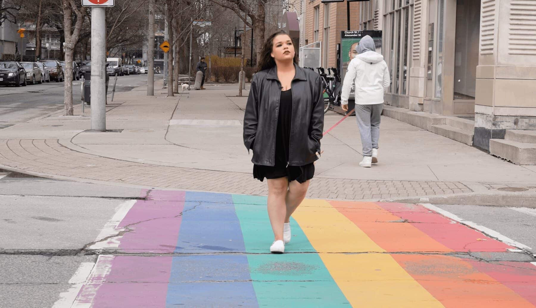 Colorful pride crosswalk on city street, diverse pedestrians, urban environment, Toronto sidewalk scene, LGBTQ+ friendly area in downtown Toronto.
