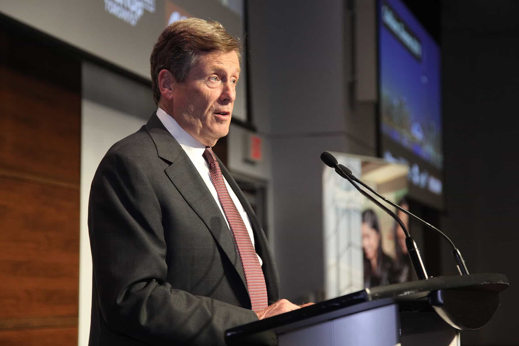 Official at a conference giving a speech in Toronto, Ontario, public speaking event, business presentation, professional speaker in a formal setting, NOW Toronto headline.
