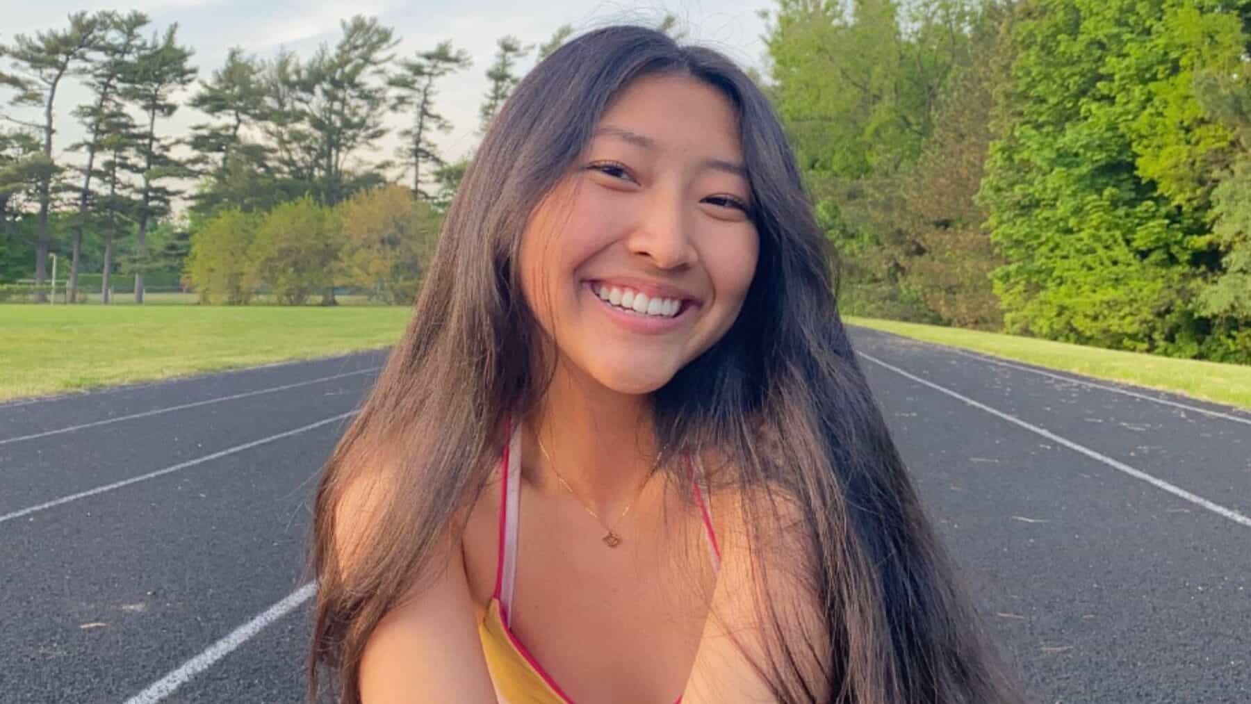 Vibrant young woman smiling outdoors on a running track with lush green trees in the background, showcasing Toronto lifestyle and outdoor activities.