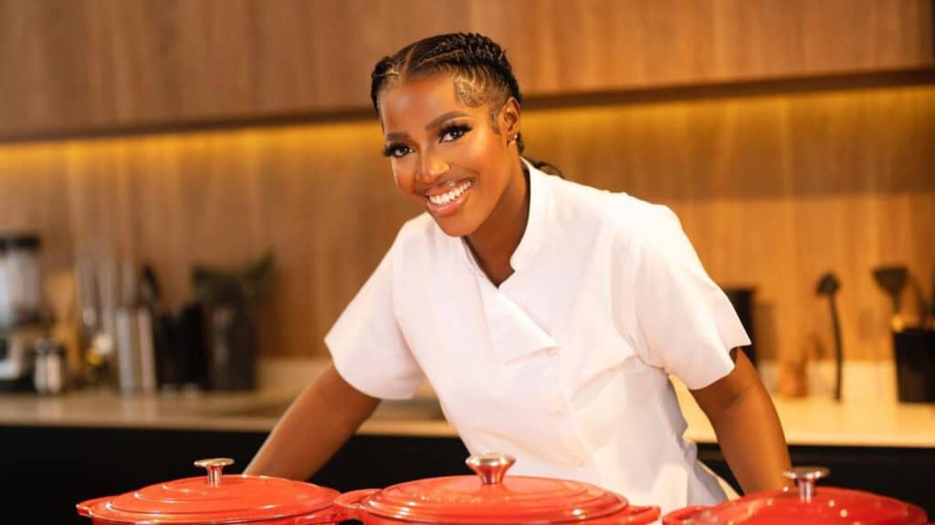 Vibrant young woman chef smiling at kitchen counter with red cookware, showcasing Toronto's diverse culinary scene and vibrant food culture.