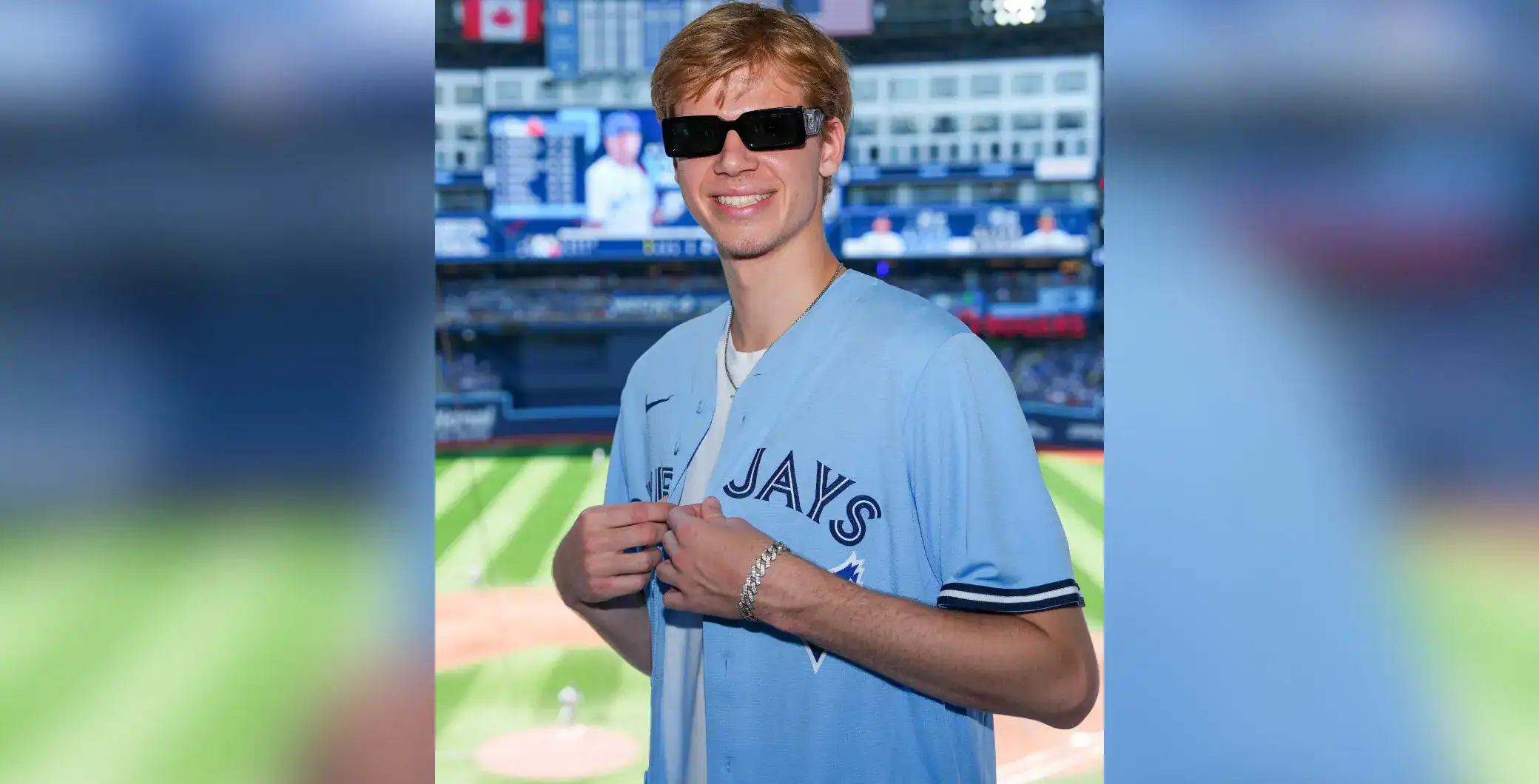 Young man at Toronto Blue Jays game wearing sunglasses and team jersey, smiling indoors with a baseball stadium background.