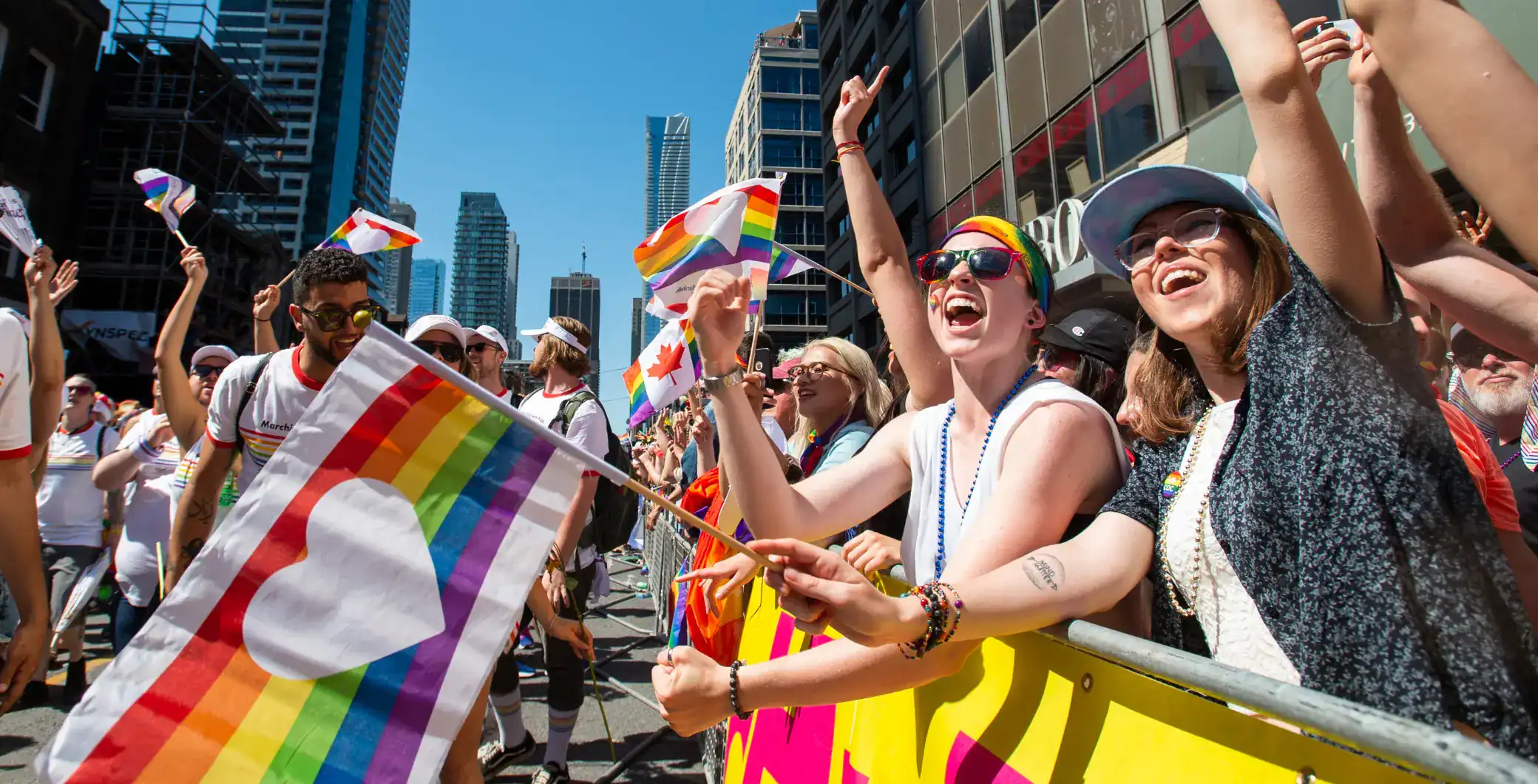 Vibrant LGBTQ+ pride parade in downtown Toronto with diverse group of joyful participants waving rainbow flags and celebrating equality under sunny skies.