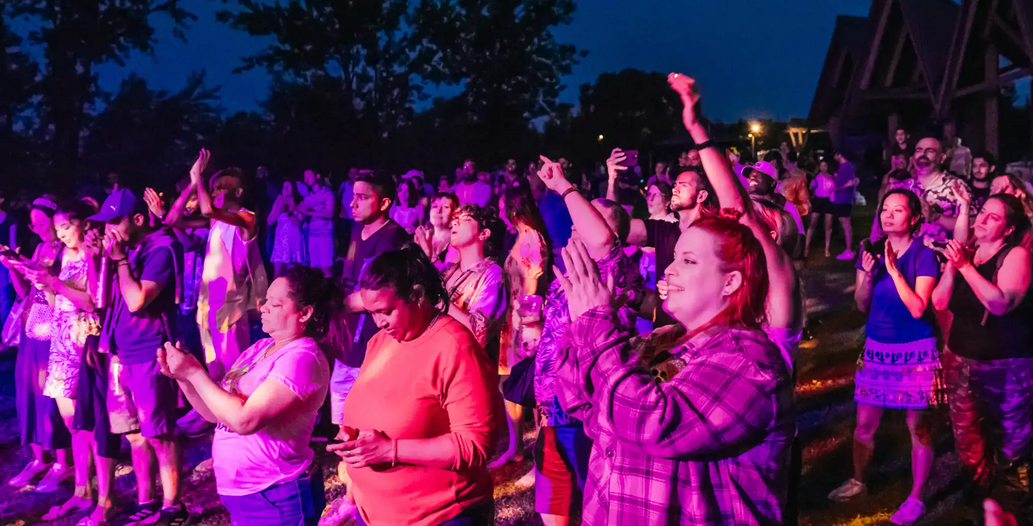 Night outdoor concert in Toronto with diverse crowd enjoying live music and dancing under vibrant purple lighting.