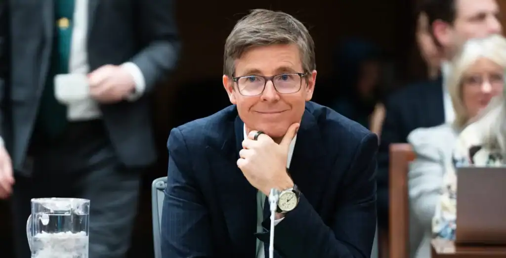 Thoughtful man wearing glasses at a conference, surrounded by professionals, reflecting Toronto's business and cultural scene, showcasing leadership and innovation.