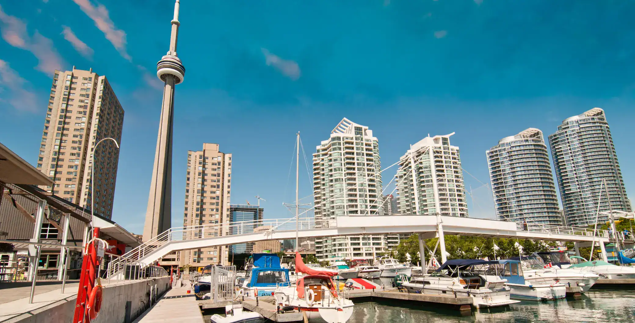 Modern Toronto skyline featuring high-rise buildings and the CN Tower near the waterfront with boats and marina.