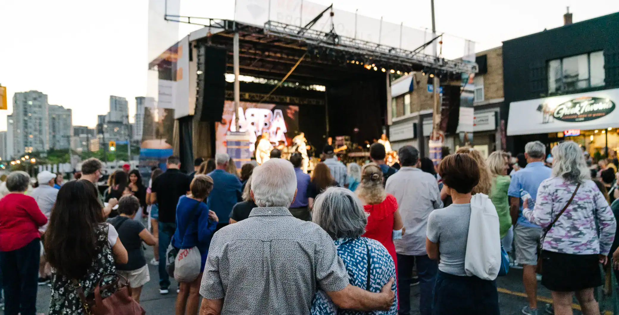 Crowd enjoying outdoor concert on city street in Toronto at sunset, lively community event, diverse audience, live music performance, urban entertainment in Toronto downtown.
