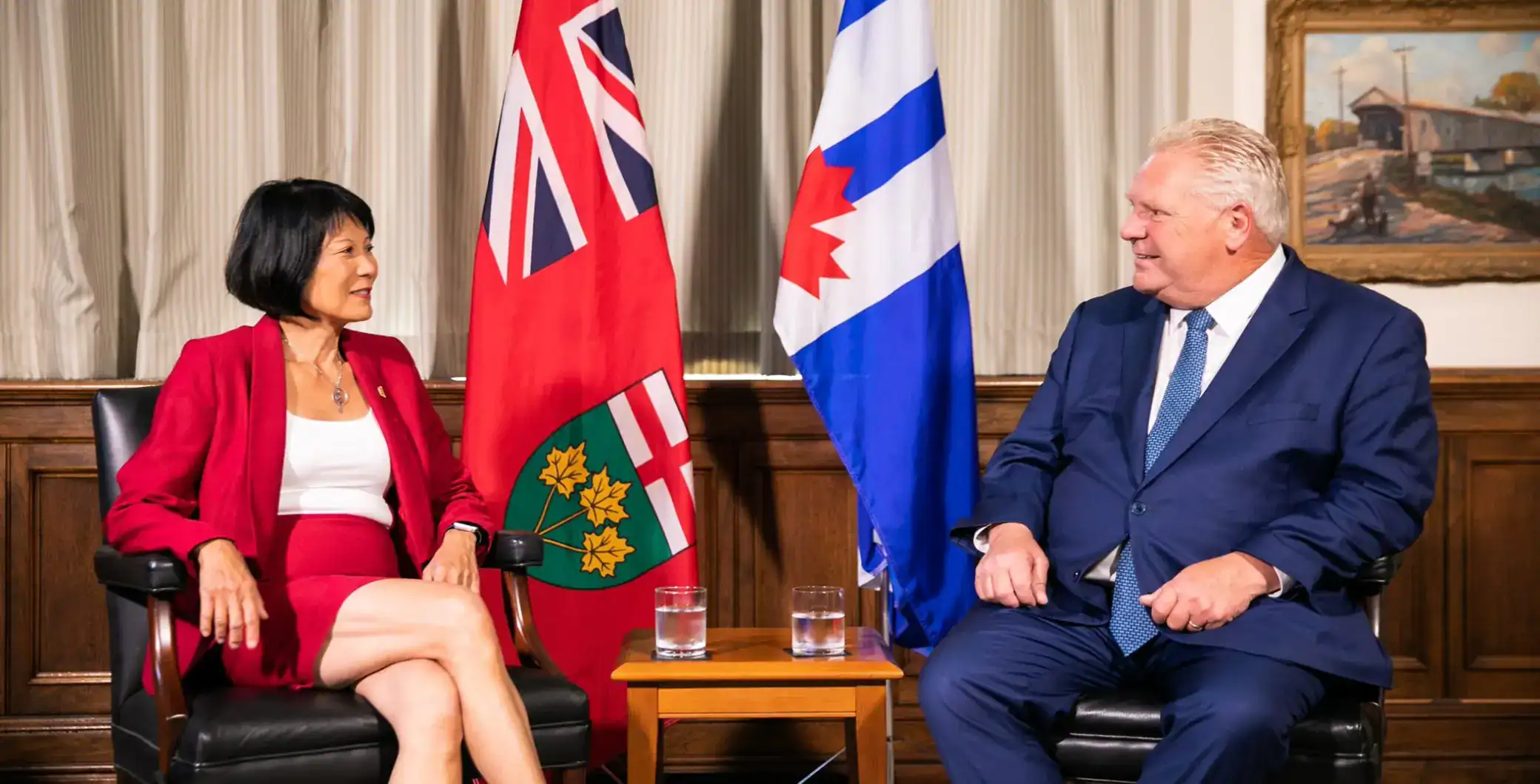 Canadian politician and diplomat meeting with a foreign leader in an official setting featuring national flags in the background.