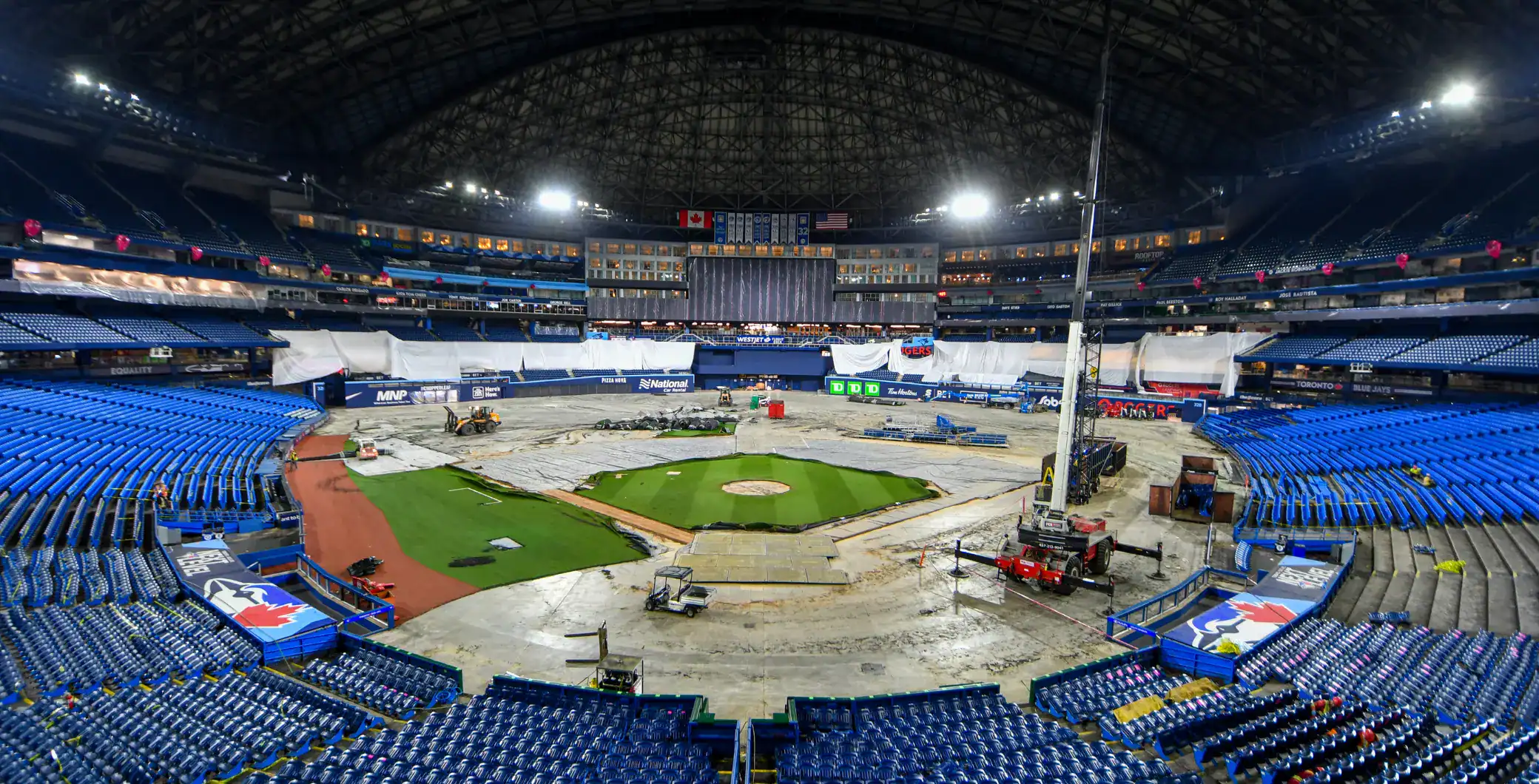 Empty Toronto Blue Jays stadium during construction or renovation work, with blue seating and a partially covered field.