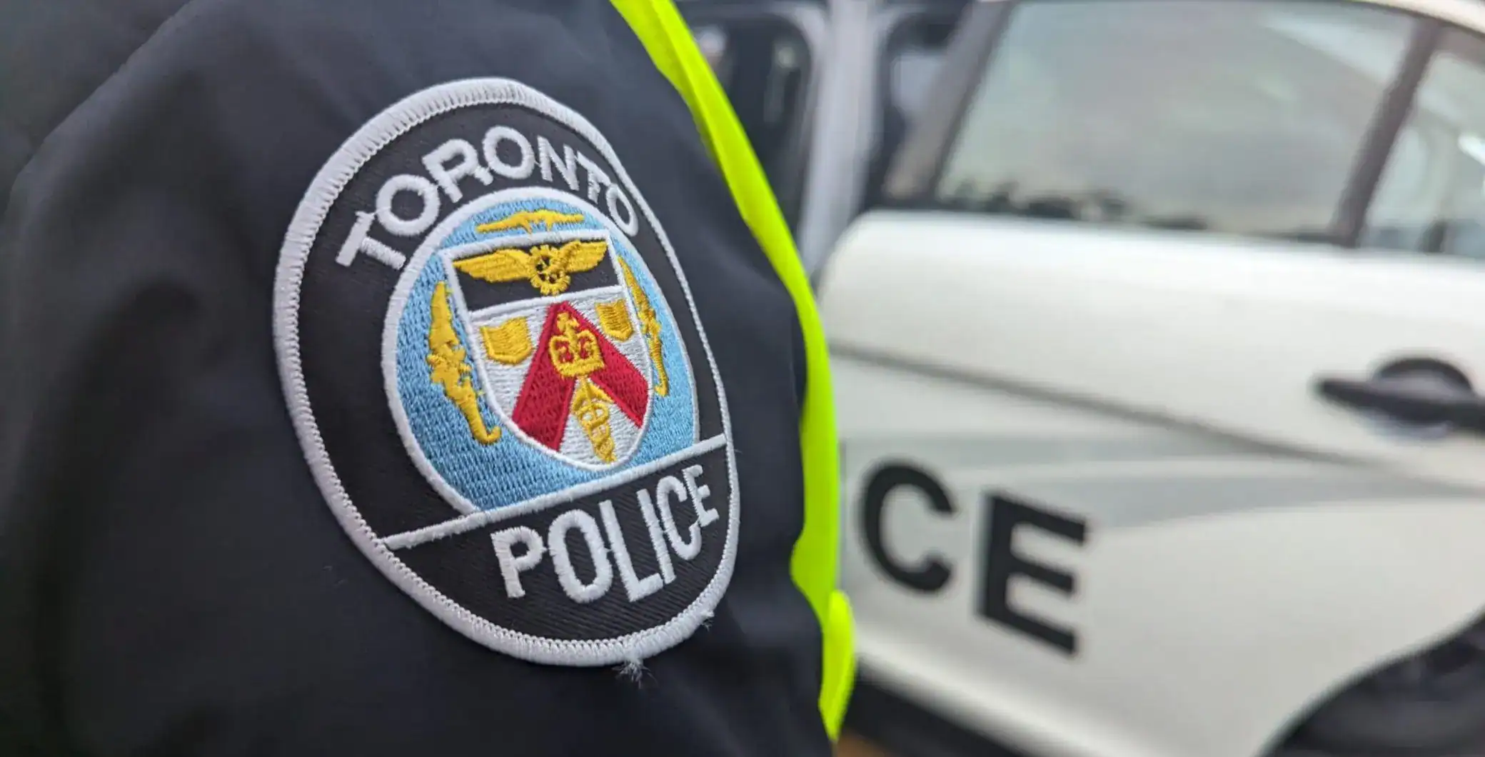 Toronto police badge on officer's uniform with police vehicle in background, Toronto law enforcement personnel, crime prevention, community safety, Toronto policing.