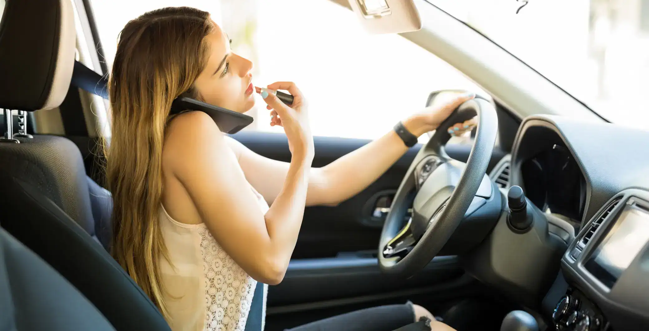 Young woman applying lipstick while talking on the phone inside a car in Toronto.