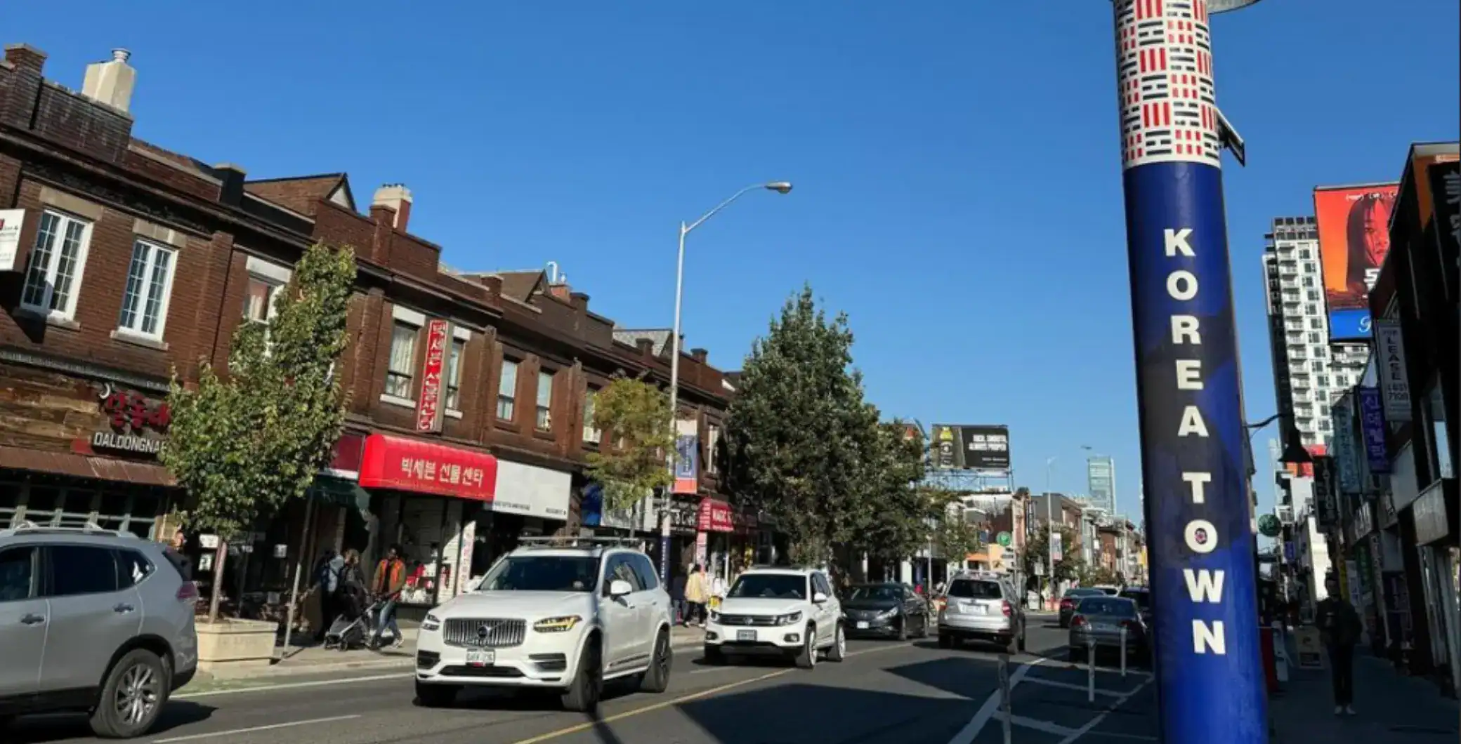 Vibrant street scene in Koreatown Toronto with local businesses, modern vehicles, and street signage under clear blue skies.