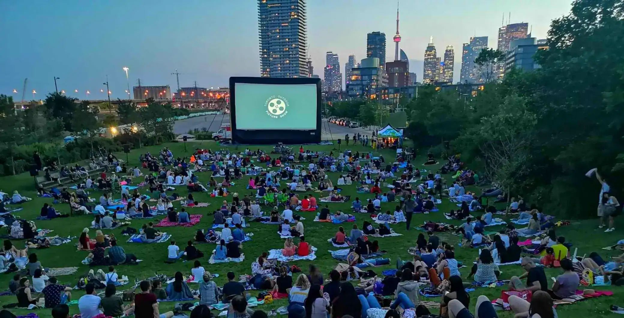 People watching outdoor movie screening in Toronto outdoor cinema park with skyline view.