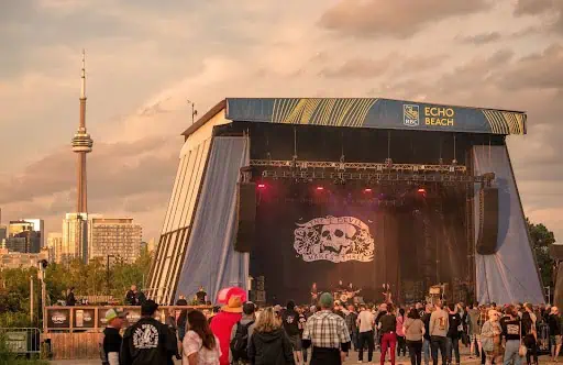 Vibrant outdoor music festival at Echo Beach in Toronto with a large stage and crowds enjoying live performances under a sunset sky.