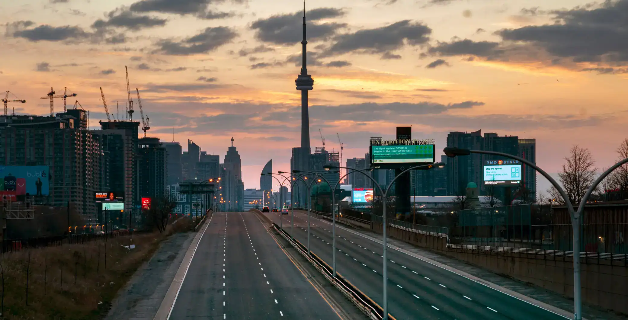 Empty highway in downtown Toronto at sunset, city skyline with CN Tower, modern buildings, and digital billboards, showcasing urban life and cityscape views.
