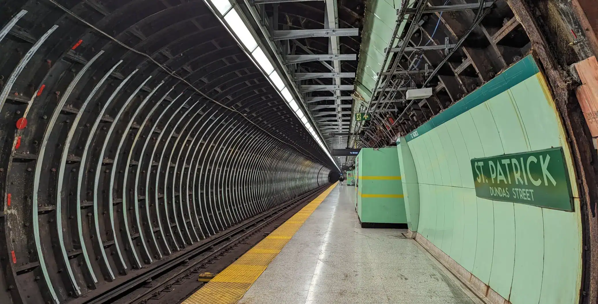 Empty Toronto subway station platform with underground tunnel walls and green signage.