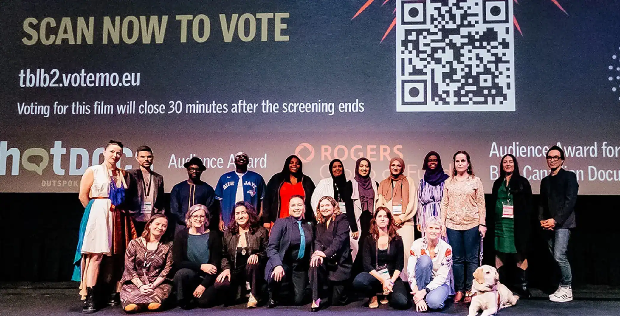 Diverse group of people on stage at the Toronto film event, highlighting inclusivity and community engagement in the Toronto film industry, with a large movie screening backdrop.