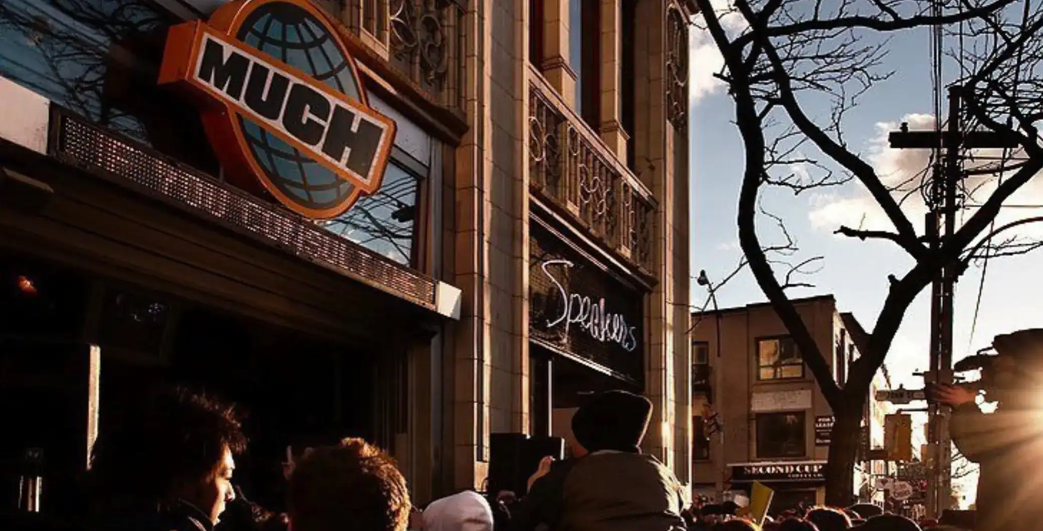 Bright street scene in Toronto showing the MUNCH sign and crowd outside a live music venue. Featuring urban architecture, leafless trees, and warm sunset lighting, capturing city culture and nightlife.