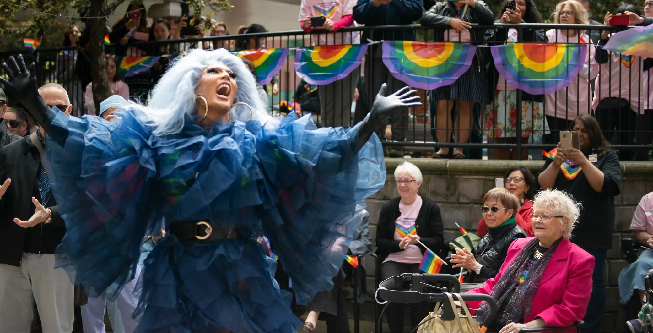 Vibrant pride parade with drag performer in colorful costume performing for cheering crowd under rainbow decorations in Toronto.
