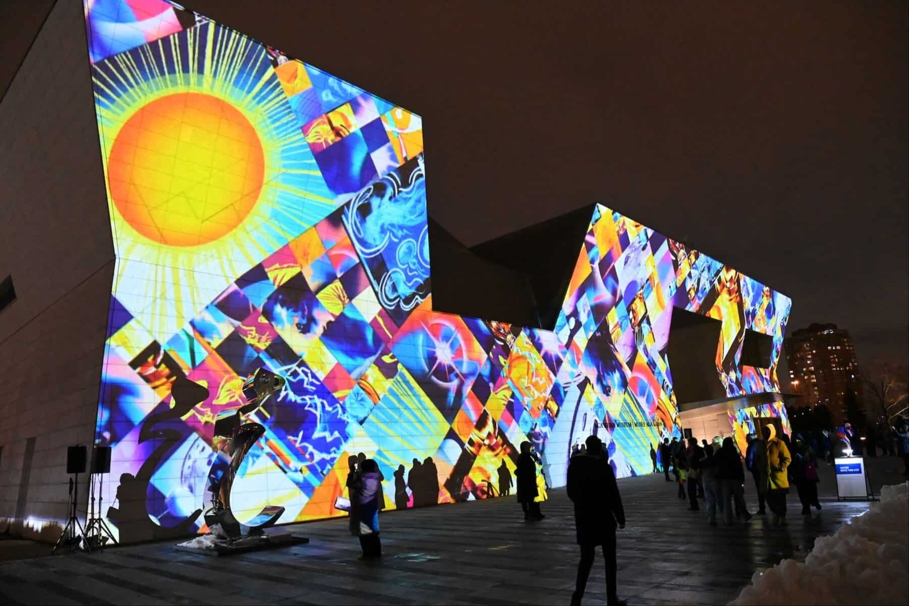 Vibrant digital art installation on the exterior of the Museum of Contemporary Art Toronto (MOCA) illuminated at night, showcasing colourful abstract projections and attracting visitors.