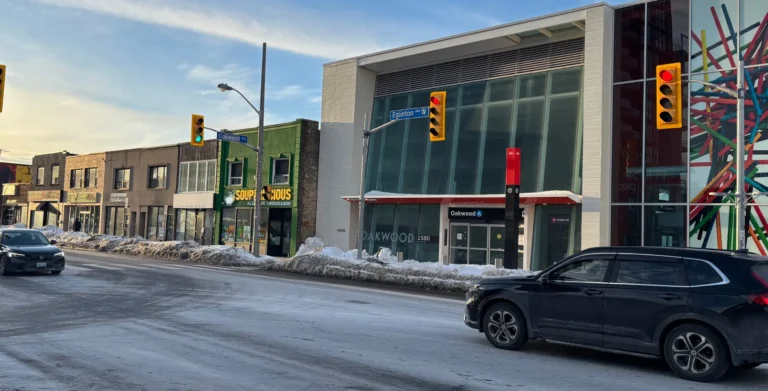 A vibrant street scene in Toronto featuring modern retail stores, traffic lights, and a snowy sidewalk, showcasing urban life and commercial activity in the city.