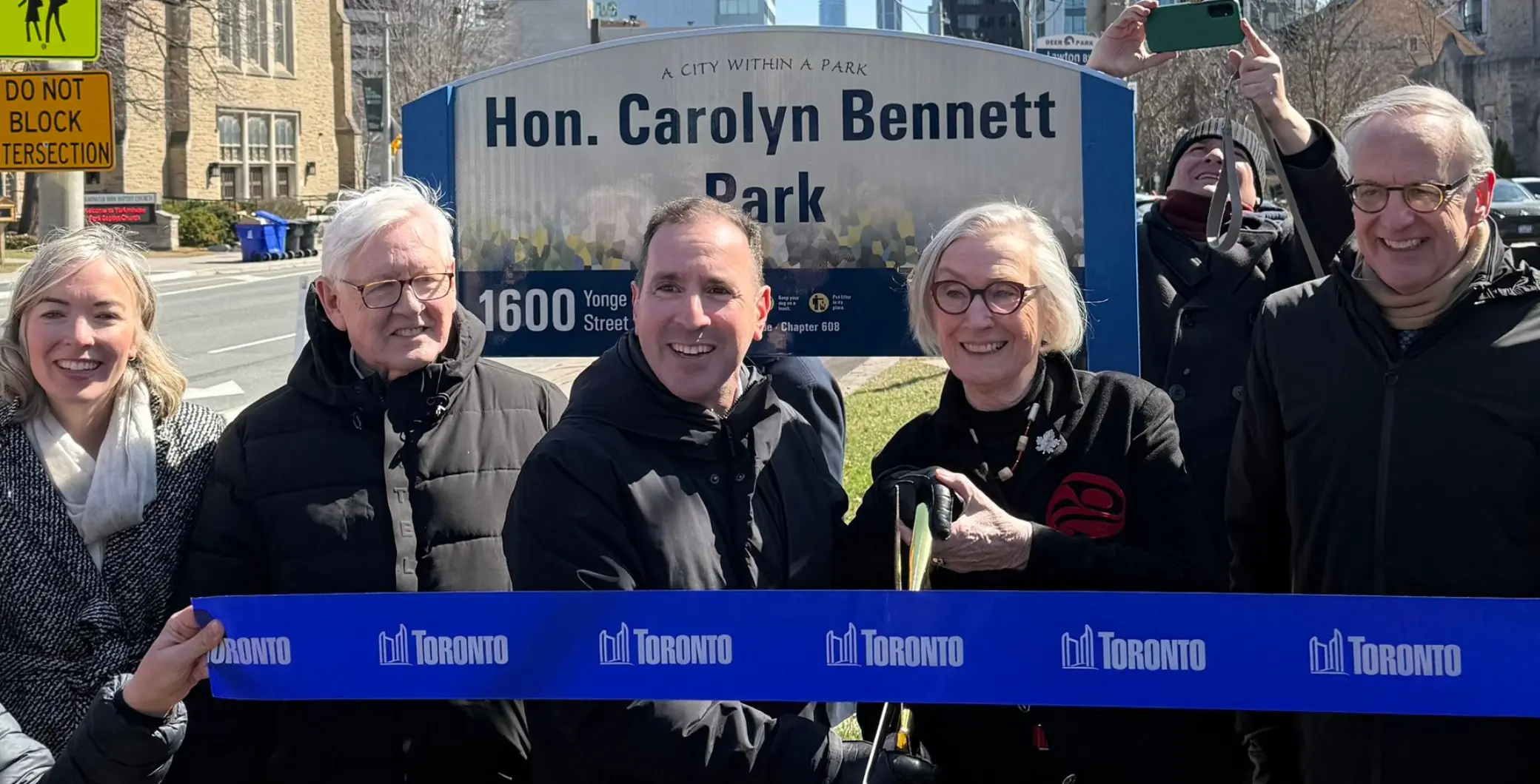 Group of people celebrating the naming of Hon. Carolyn Bennett Park in Toronto, with a sign and ribbon-cutting ceremony, highlighting community recognition and urban development.