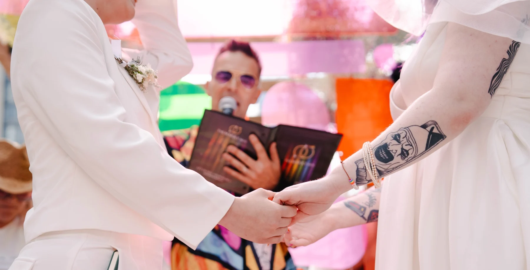 Two individuals holding hands during a same-sex wedding ceremony at Toronto Pride weekend, with a celebrant officiating in the background.