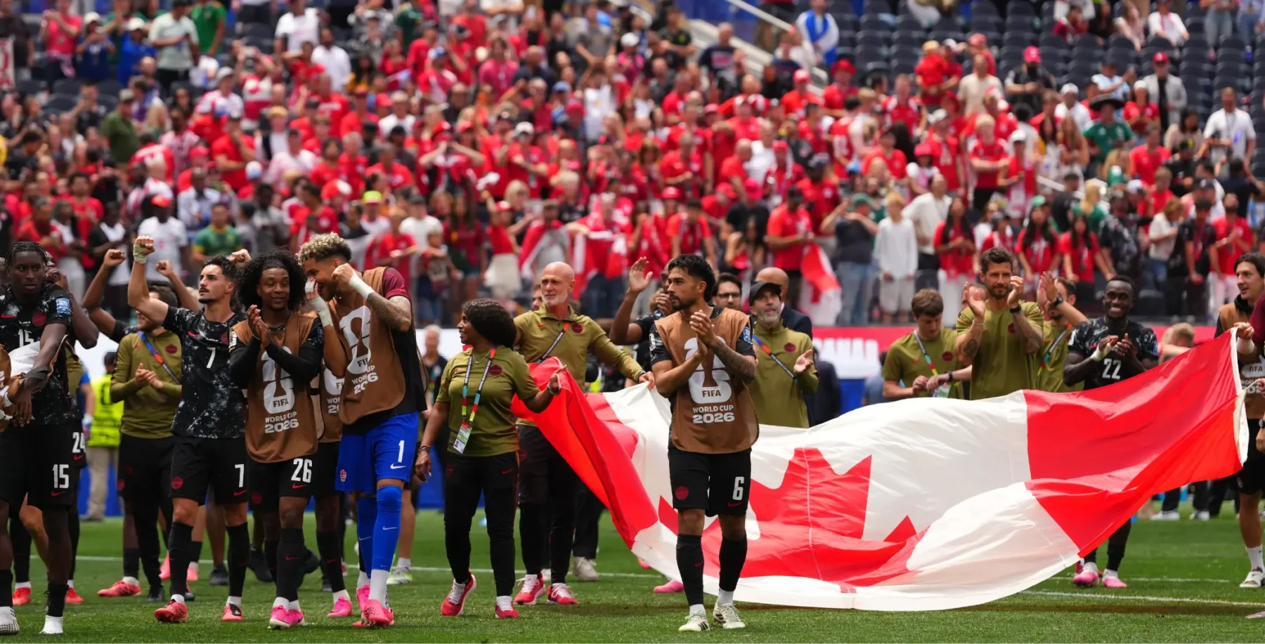 Canadian soccer players celebrate on the field with a large Canadian flag after advancing to the World Cup Round of 16.