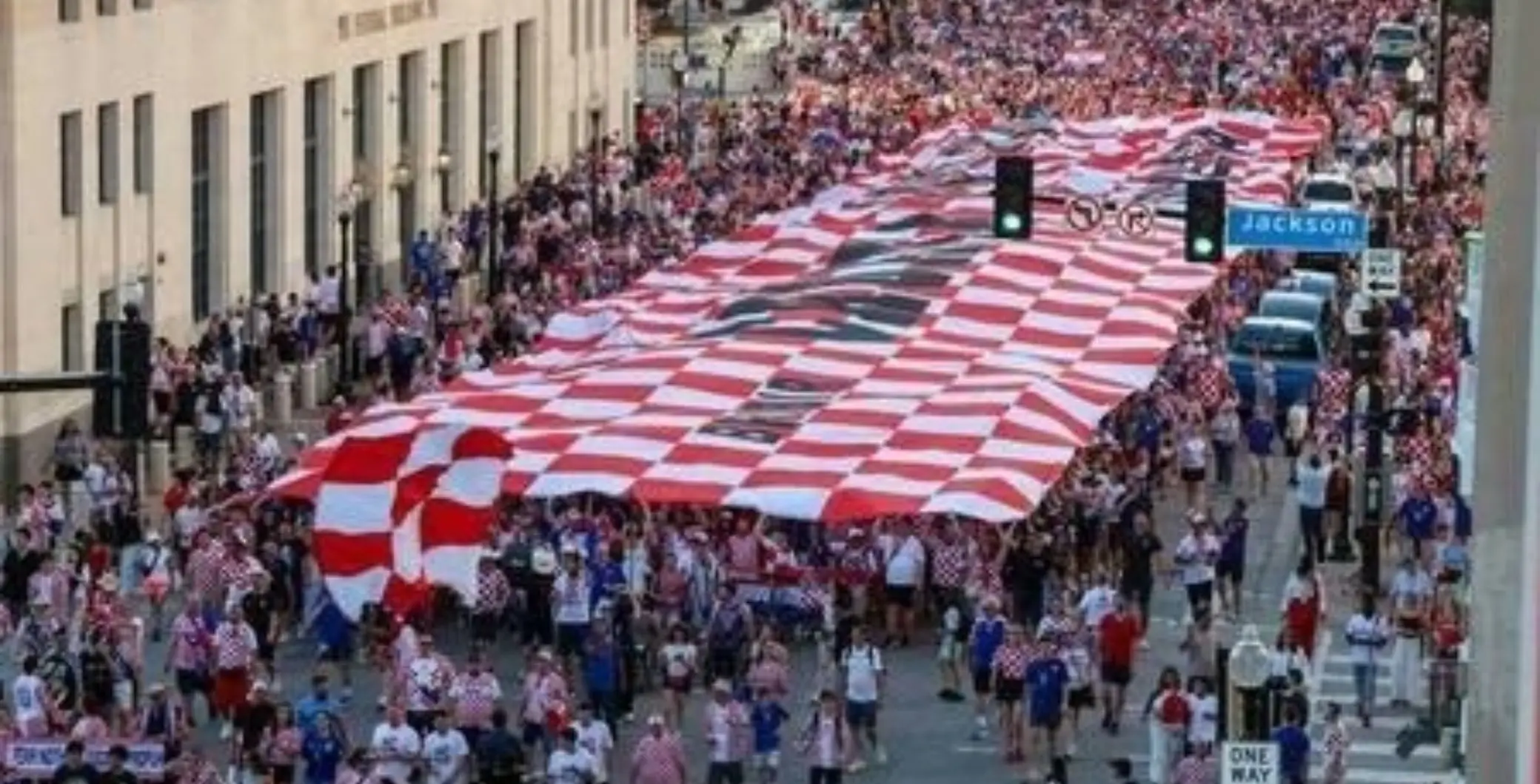Large crowd participating in a parade with a giant red and white checkered fabric float in downtown Toronto, surrounded by spectators and city buildings.