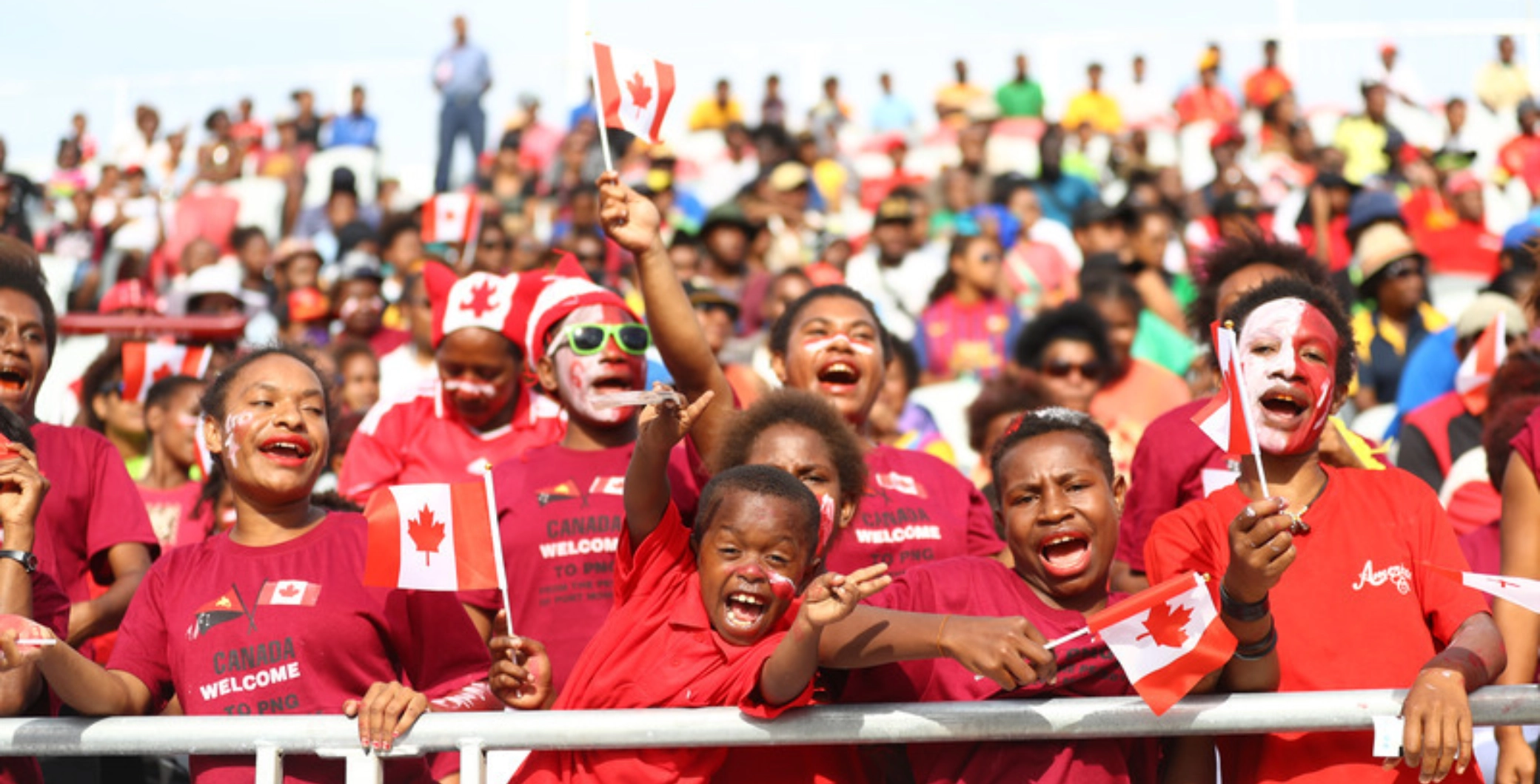 Toronto fans, including children, cheer and wave Canadian flags at FIFA Fan Fest event, showing excitement and national pride during the World Cup.