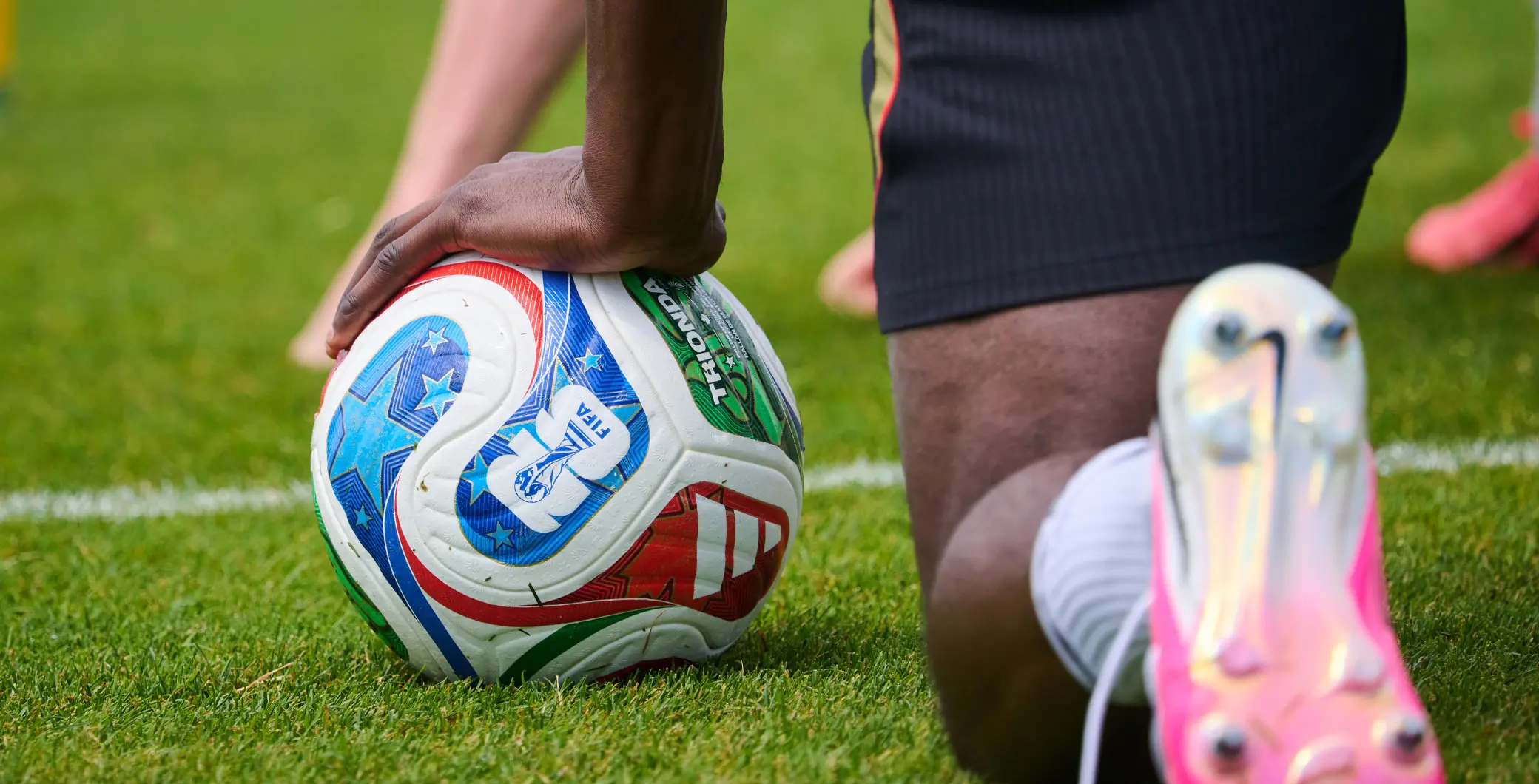 A rugby player preparing to kick the ball on a grassy field, close-up shot focusing on the player's legs and the rugby ball, with a blurred background.