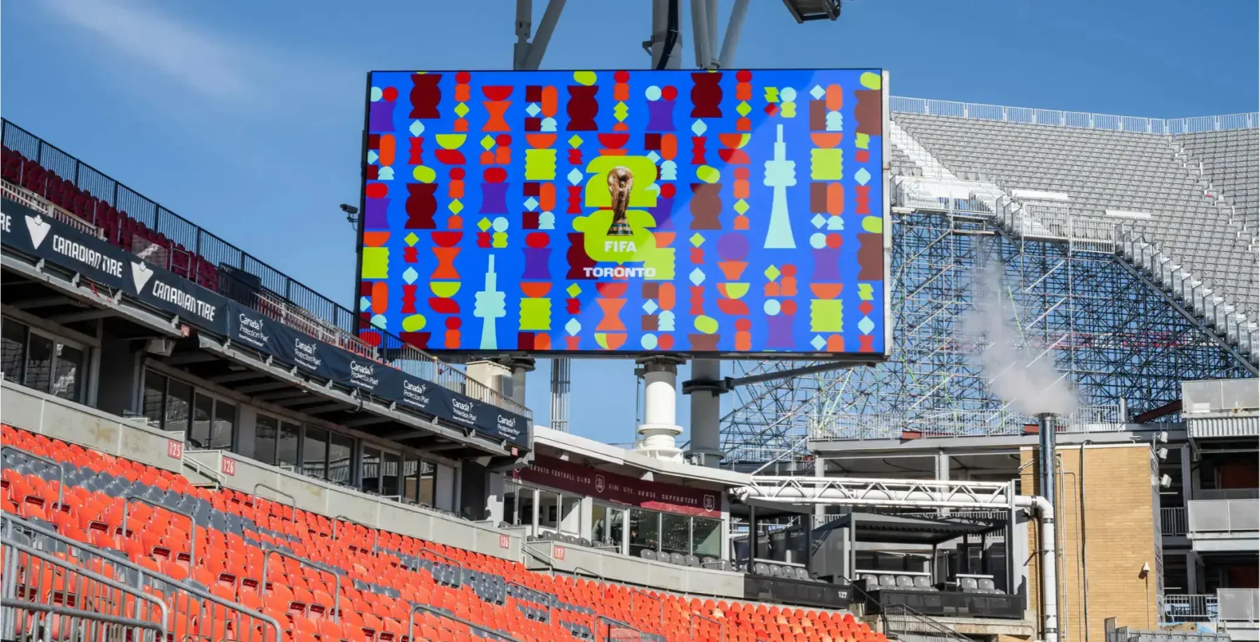 A vibrant digital billboard at Toronto's stadium displaying colorful graphics and the FIFA World Cup logo, with empty stadium seats in the background, highlighting Toronto's sports and event scene.