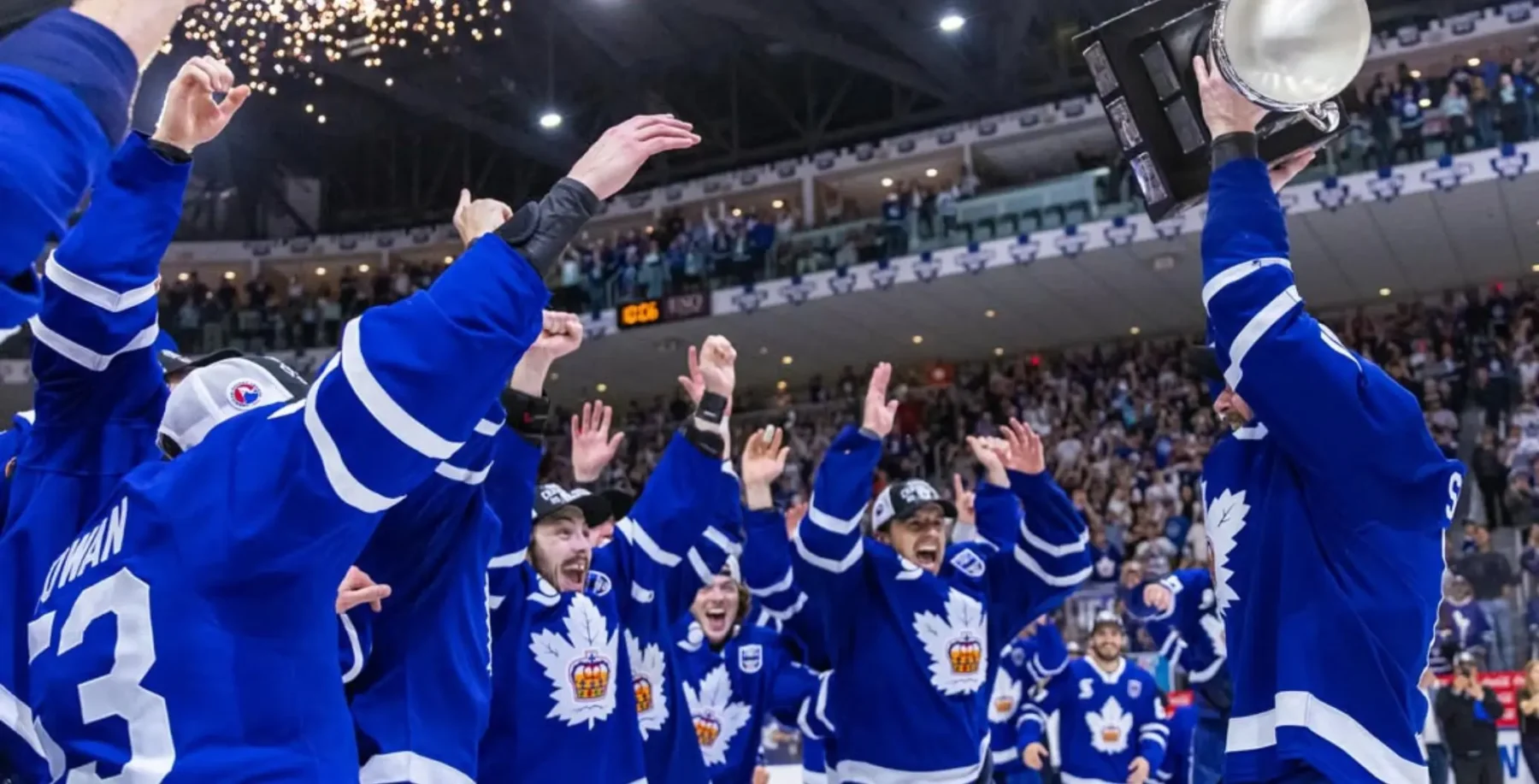 Toronto Marlies players celebrate their Calder Cup victory with fans at a rally, raising their hands in triumph in the arena.