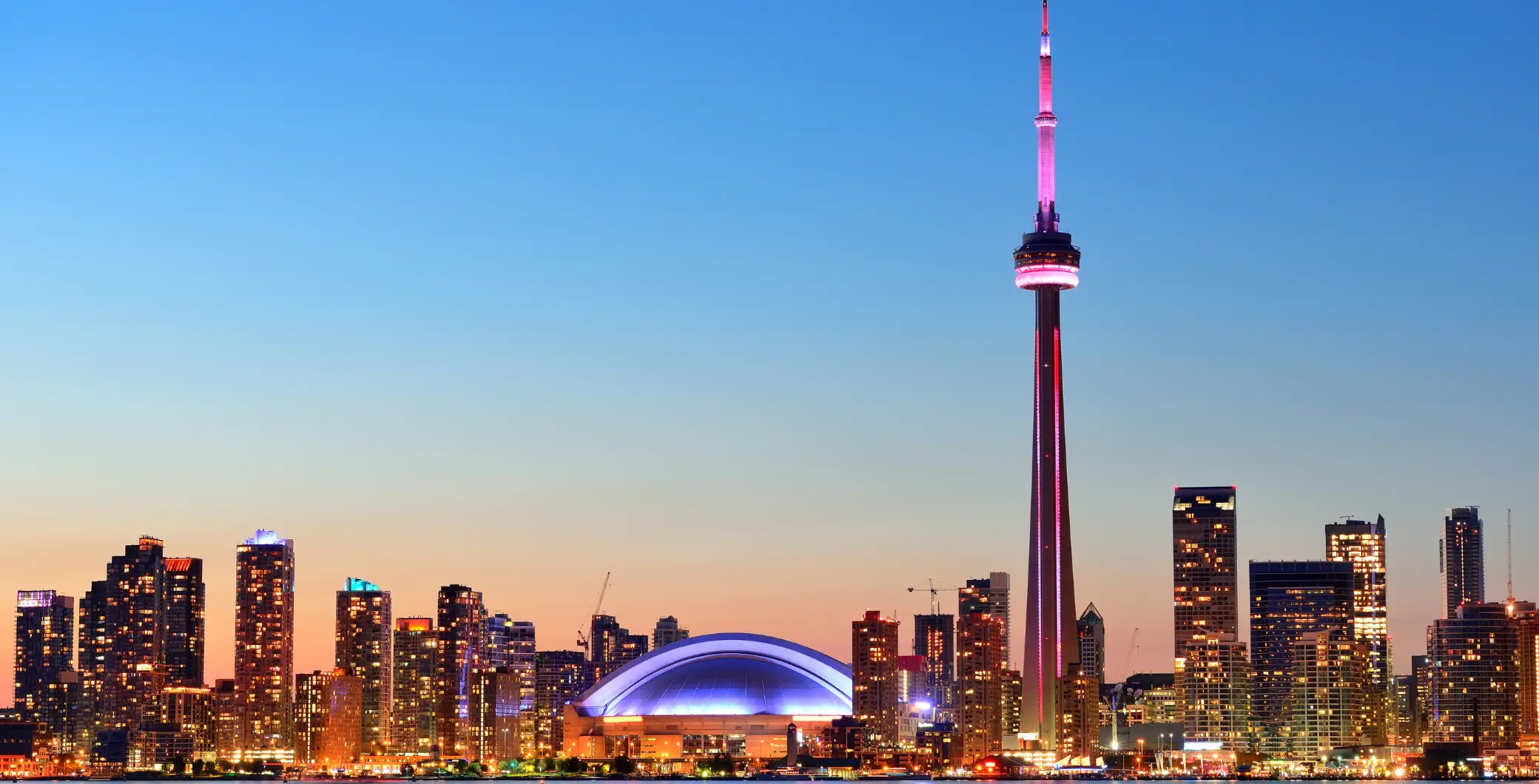 Toronto skyline at dusk featuring the CN Tower and Rogers Centre, highlighting the city's vibrant urban landscape and iconic landmarks.