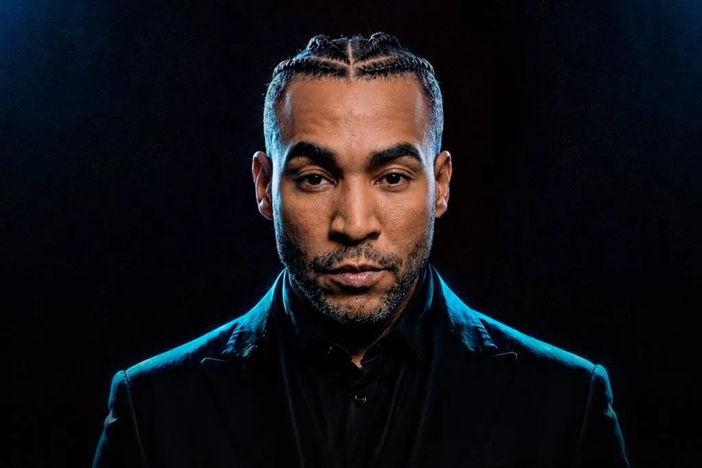 Portrait of Don Omar with braided hair, wearing a dark suit against a black background, promoting his 'The Last King World Tour'.