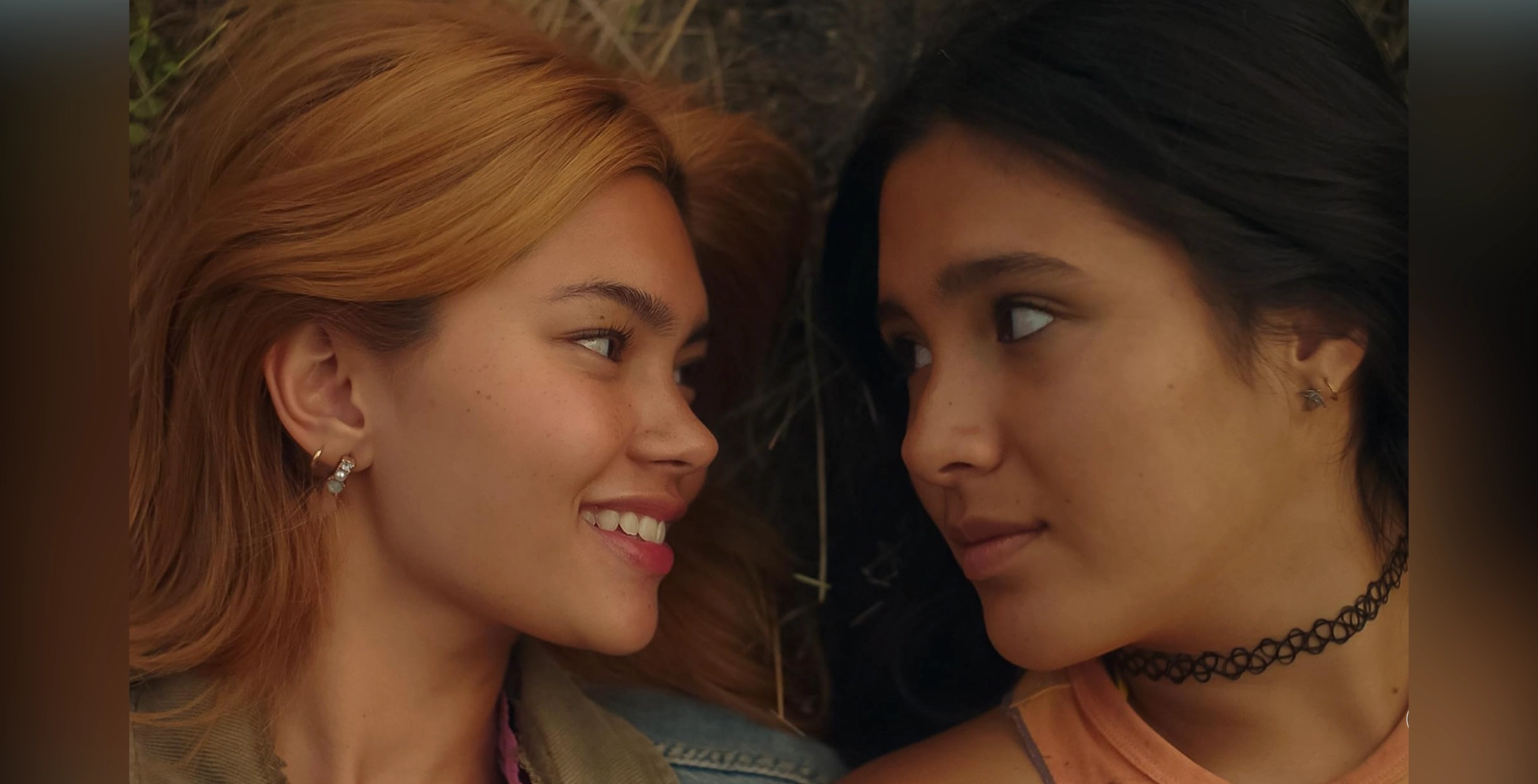 Two young women with contrasting hair colors face each other closely, smiling and sharing an intimate moment.