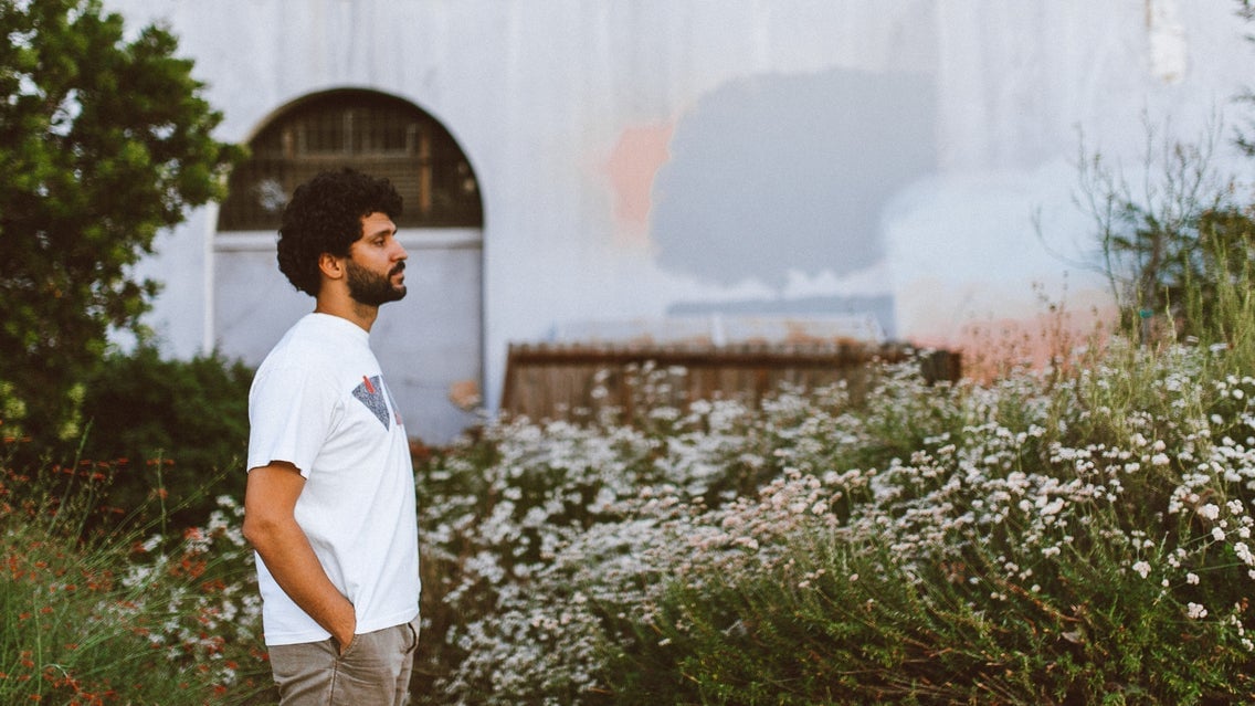 Kiefer standing outdoors among wildflowers with a white building in the background, capturing a contemplative moment in Toronto.