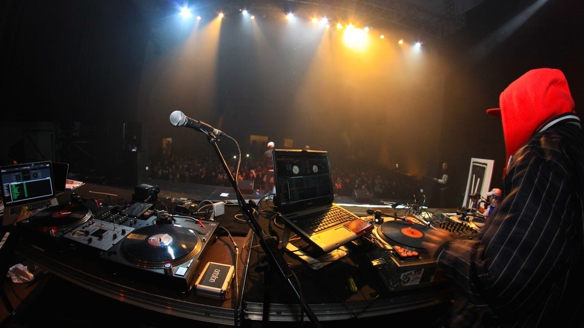 DJ performing live on stage with turntables and equipment at a concert, vibrant stage lighting illuminating the scene.