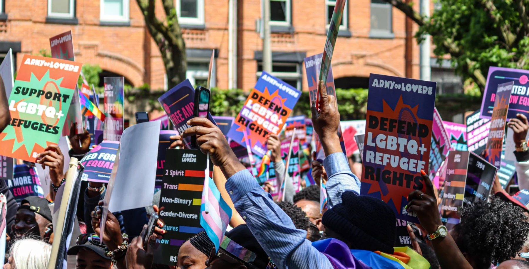 Protesters hold signs supporting LGBTQ+ refugees at a rally, advocating for better rights and support in Canada.