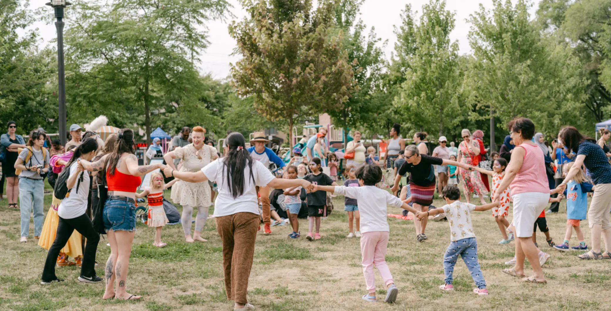 Community outdoor festival in Etobicoke with families dancing and children playing in a park setting.