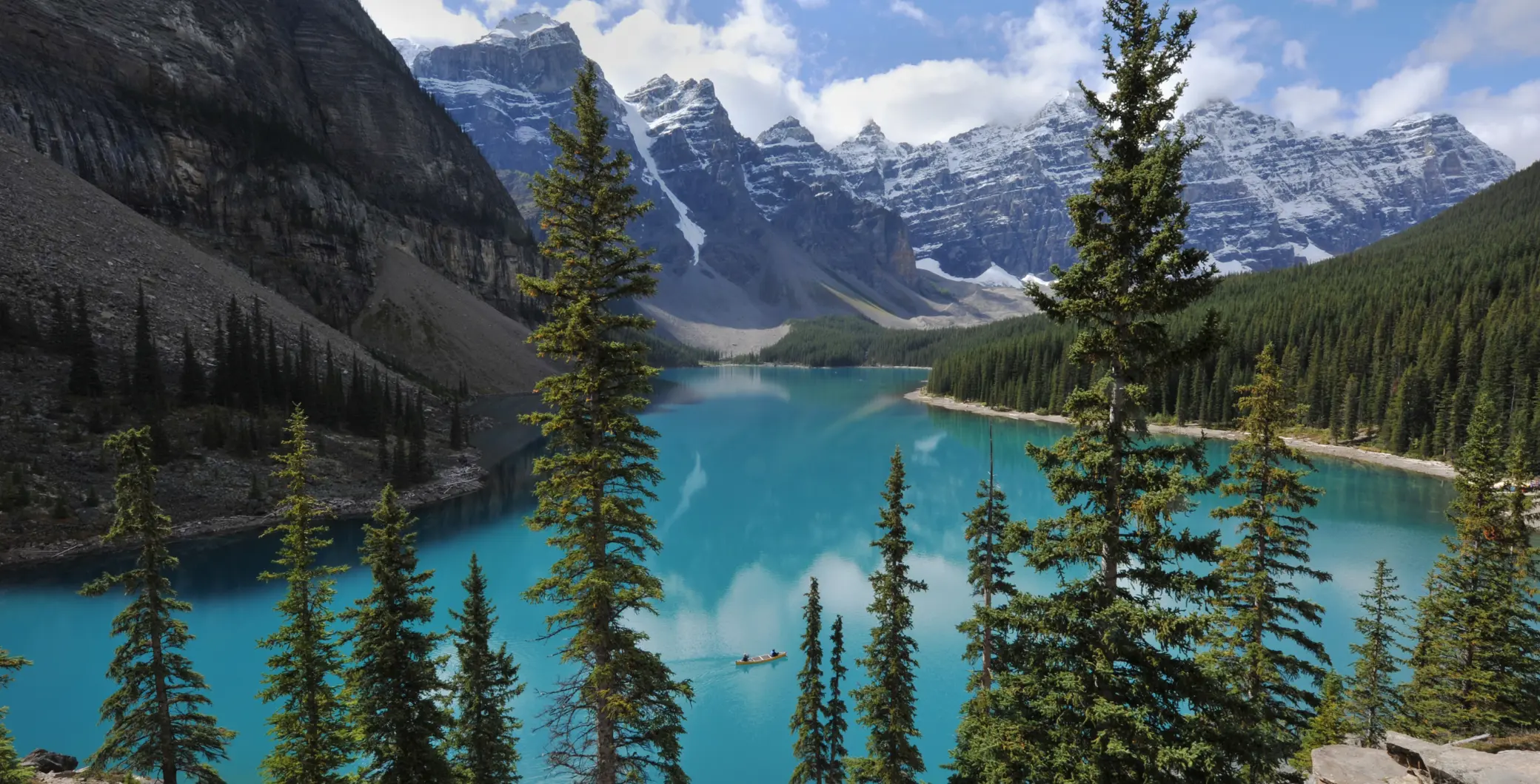 Scenic view of turquoise lake surrounded by evergreen trees and snow-capped mountains in Ontario, Canada.