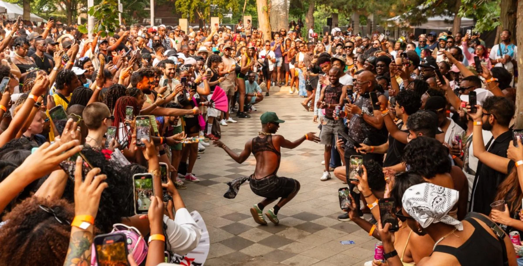 Black Queer dancer performing joyfully during Toronto Caribbean Carnival weekend with a large crowd watching and capturing the moment.