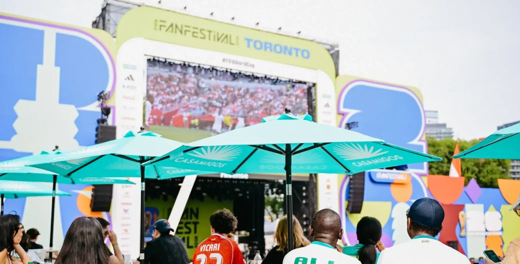 Crowd gathered at Toronto Fan Festival with large screen and colorful decorations, celebrating FIFA World Cup event.