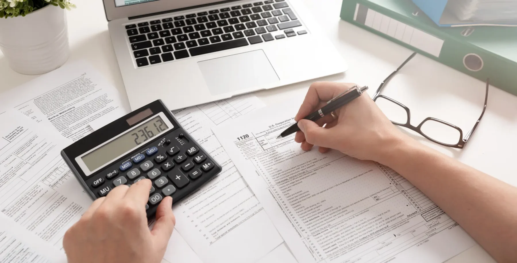 Person working with financial documents, calculator, and laptop on a desk, representing business or accounting activities in Toronto.