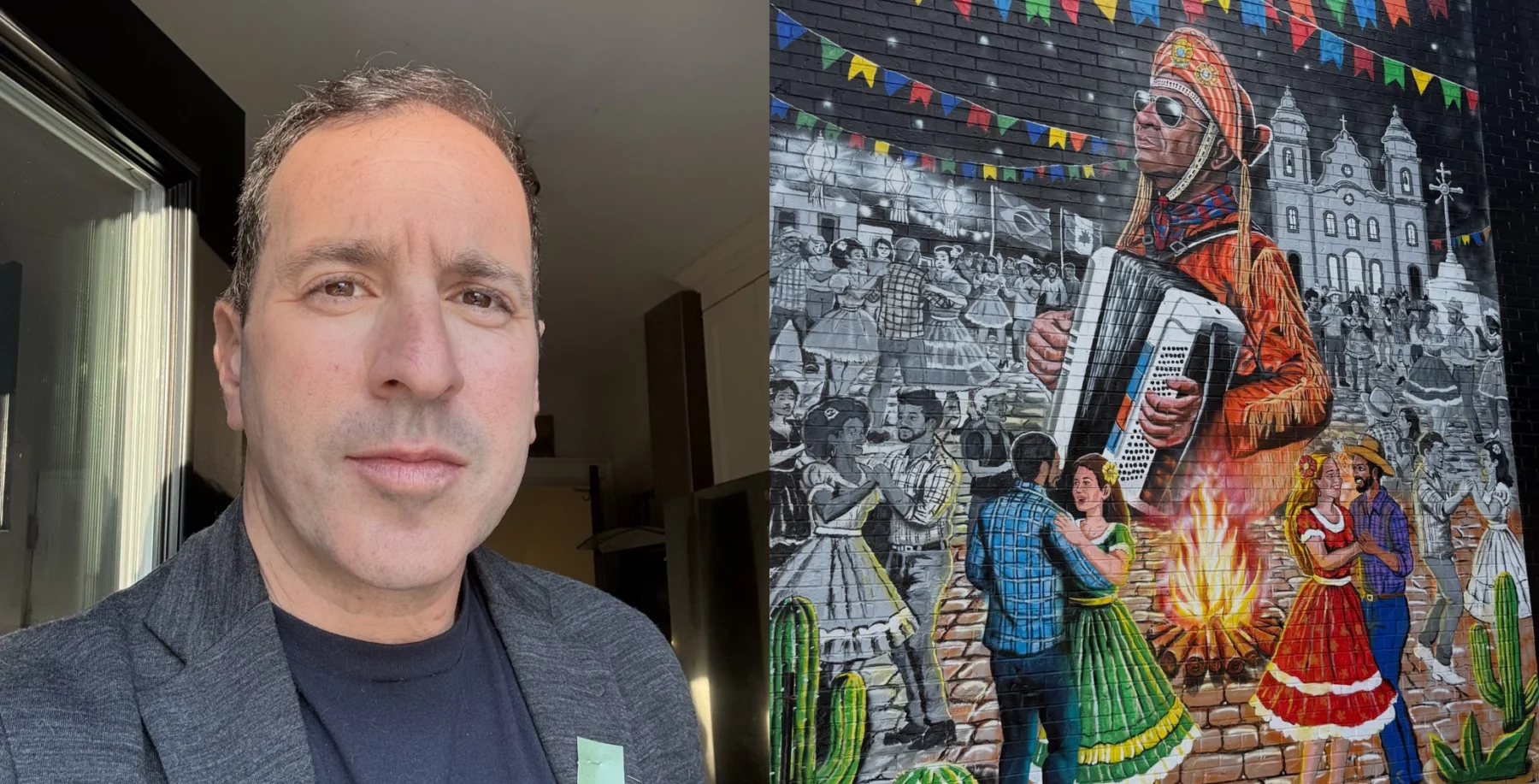 A man with short dark hair and a serious expression stands indoors near a window, wearing a dark blazer and shirt, with a mural of a musician and dancers in the background.