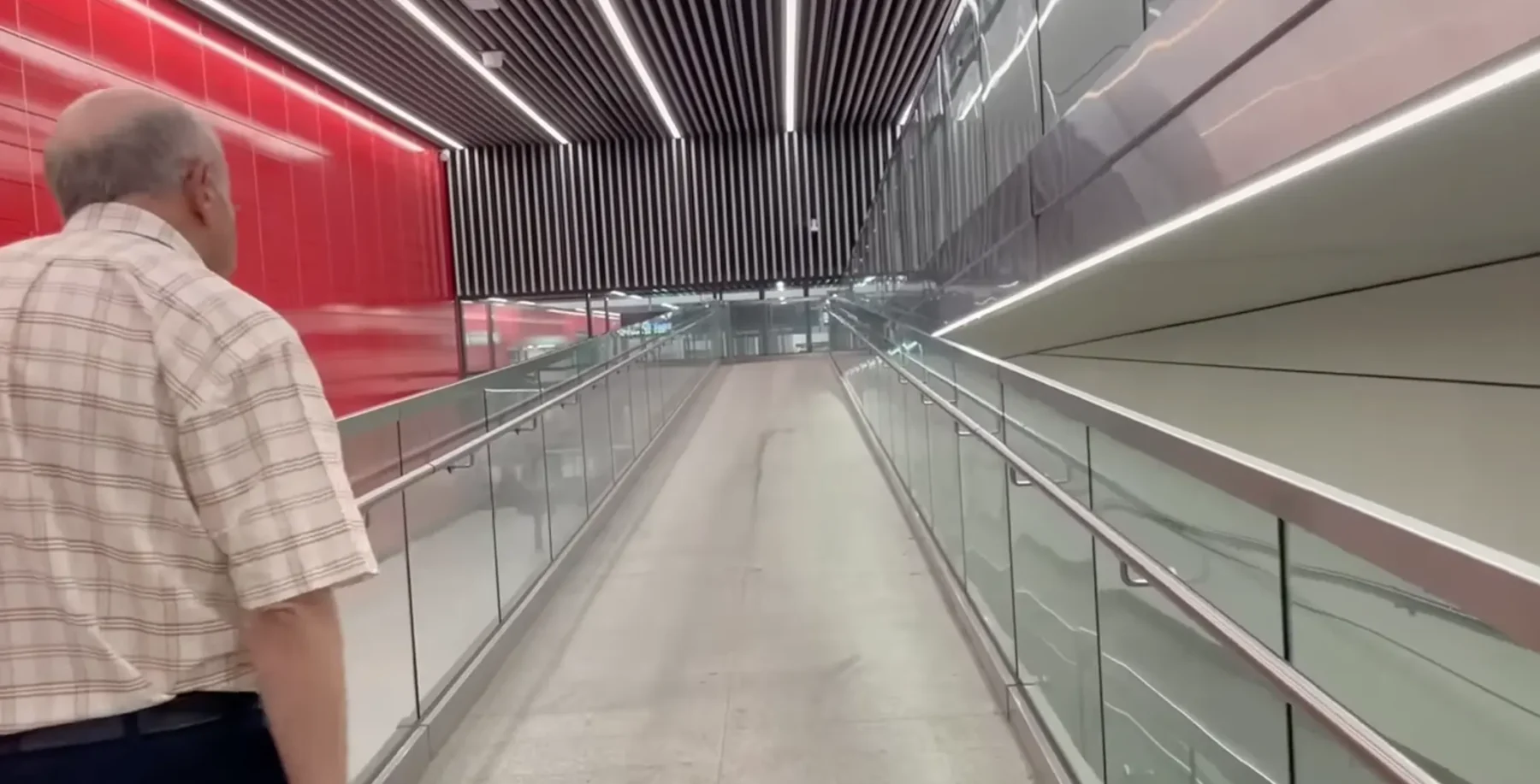 A man in a checkered shirt walking through a modern, brightly lit corridor with glass railings and sleek architectural design in Toronto.