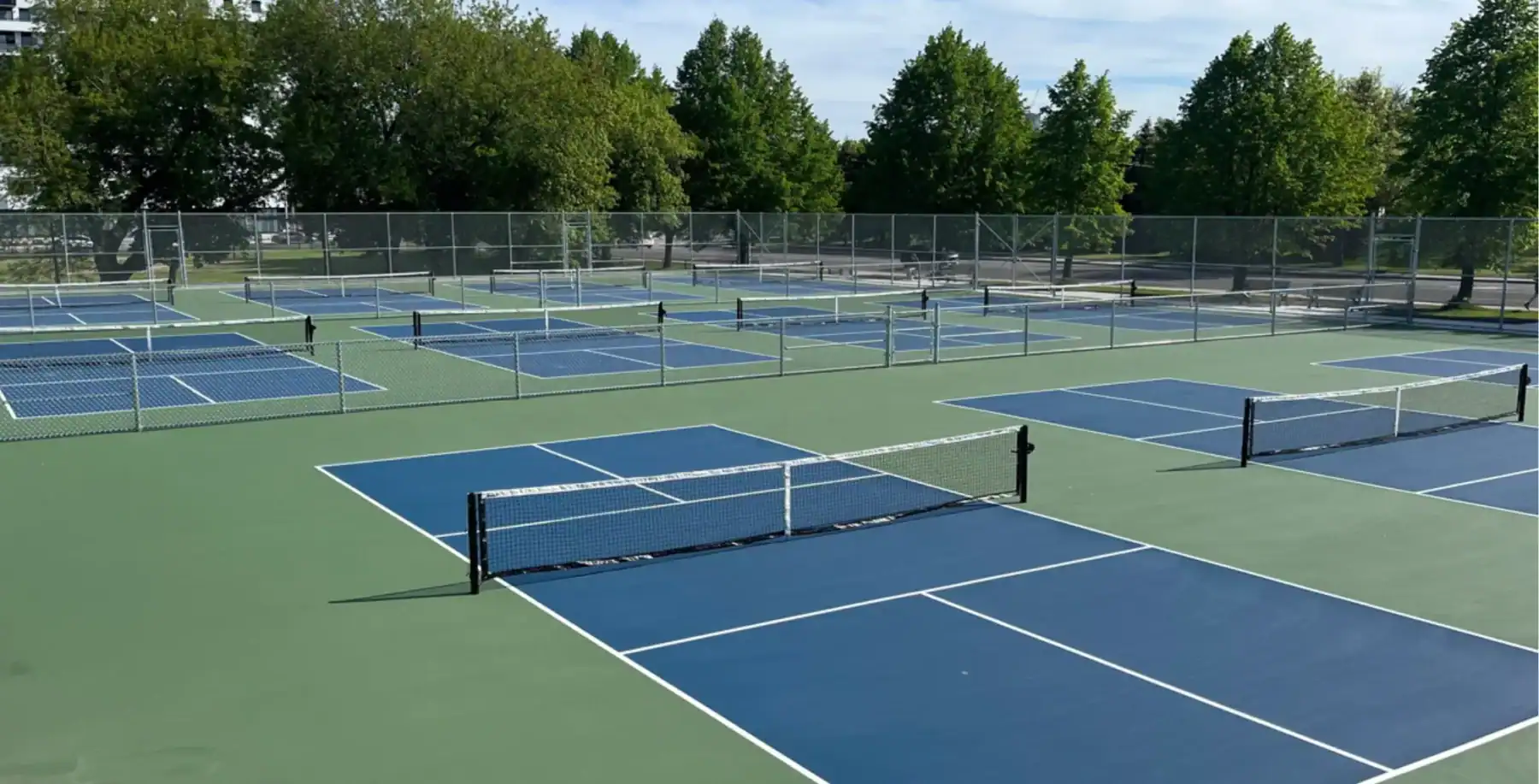 Toronto's new pickleball courts with 16 playing areas, surrounded by green trees and a clear sky, showcasing a modern sports facility.